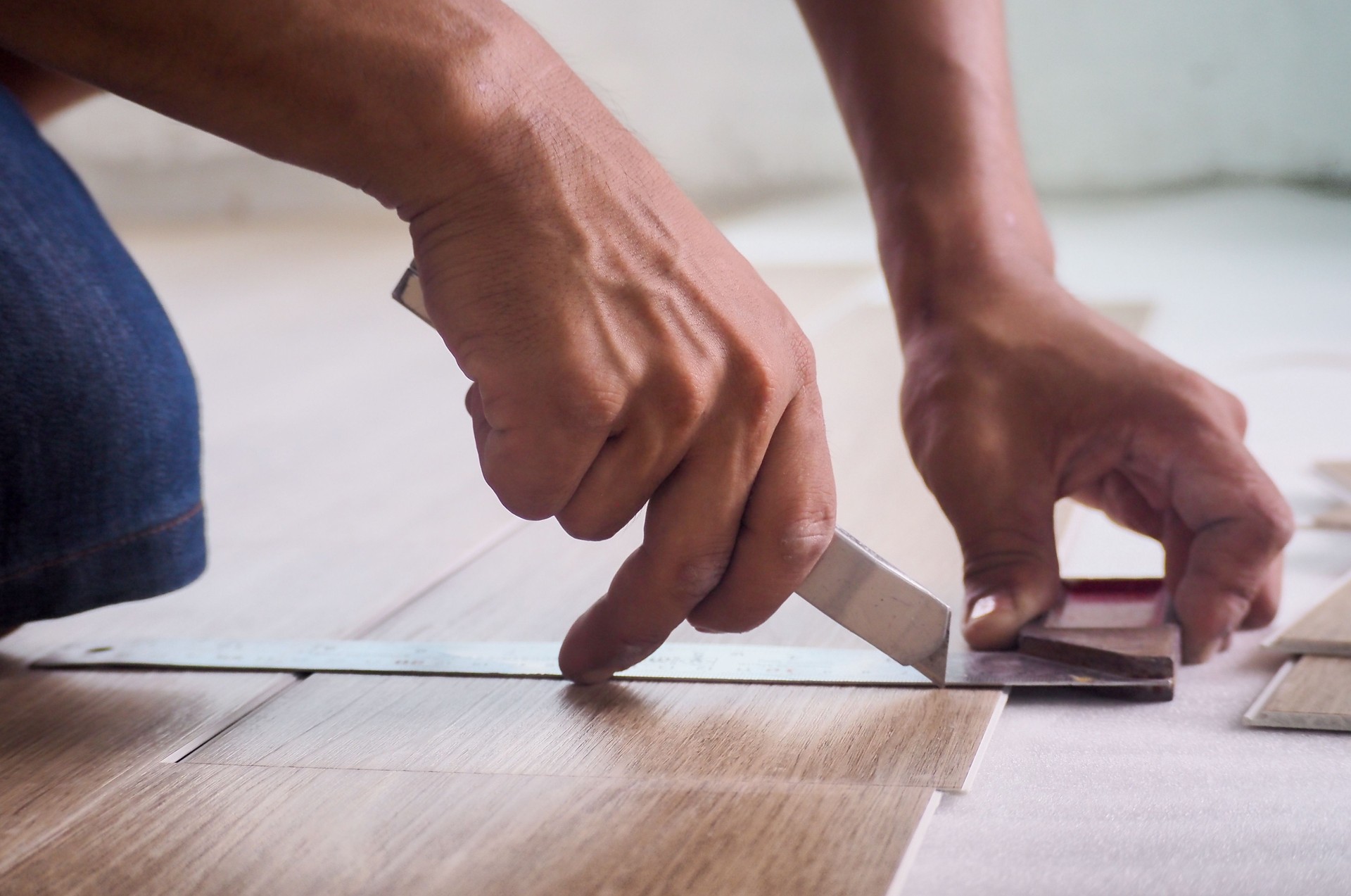 A technician is cutting luxury vinyl floor tiles with a cutter to lay the floor before placing it on the leveling foam.